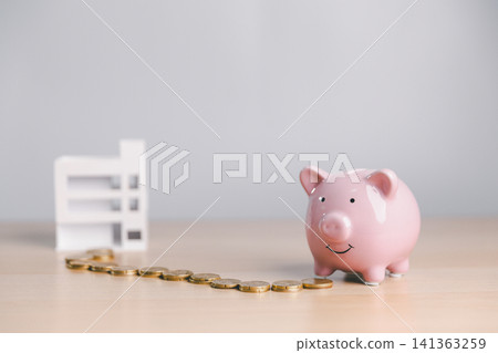 Pink piggy bank with coin path and blurred building model, symbolizing saving money for real estate, property investment goal, mortgage planning, and financial growth. Pink piggy bank with coin path and blurred building model, symbolizing saving money for real estate, property investment goal, mortgage planning, and financial growth. 141363259