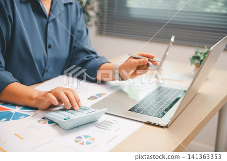 Business analyst using calculator and laptop with printed financial charts on a bright office desk, showing accounting, budget planning, data analysis, investment review, Business analyst using calculator and laptop with printed financial charts on a bright office desk, showing accounting, budget planning, data analysis, investment review, 141363353