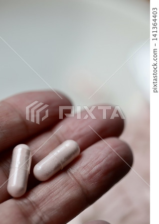 一隻手拿著一個透明膠囊,裡面裝著卡姆果粉;一種維生素補充劑。 一隻手拿著一個透明膠囊,裡面裝著卡姆果粉;一種維生素補充劑。 141364403