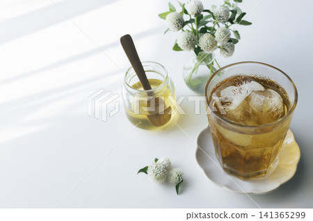 在白色的桌子上,自然光和斑駁的陽光下,冰茶和蜂蜜擺放著。 在白色的桌子上,自然光和斑駁的陽光下,冰茶和蜂蜜擺放著。 141365299