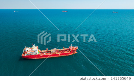 Aerial view of red tanker ship in open sea with multiple cargo vessels on horizon Aerial view of red tanker ship in open sea with multiple cargo vessels on horizon 141365649