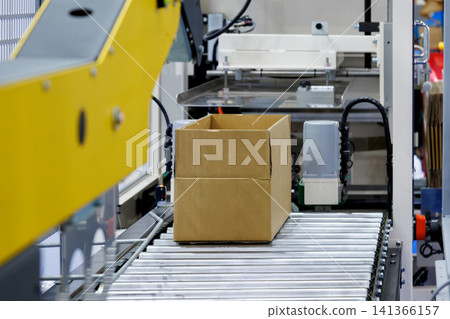 brown cardboard box on roller of conveyor belt at automatic carton sealing machine. Industrial product packaging, logistics, and e-commerce fulfillment factory automation concept brown cardboard box on roller of conveyor belt at automatic carton sealing machine. Industrial product packaging, logistics, and e-commerce fulfillment factory automation concept 141366157