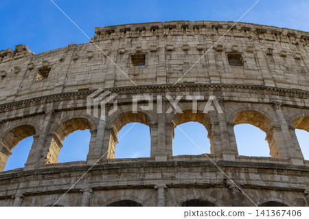 Famous Coliseum in Rome. Colosseum, or Coliseum. Part of the wall of an antique stone structure with arches. Italy, Europe. Famous touristic place in the world, Europe. Beautiful blue sky background. Famous Coliseum in Rome. Colosseum, or Coliseum. Part of the wall of an antique stone structure with arches. Italy, Europe. Famous touristic place in the world, Europe. Beautiful blue sky background. 141367406