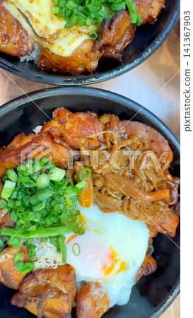 Japanese barbecue chicken rice bowl with soft poached egg, scallions, glazed grilled meat, and noodles served in black bowls on wooden table, warm rich comfort food closeup Japanese barbecue chicken rice bowl with soft poached egg, scallions, glazed grilled meat, and noodles served in black bowls on wooden table, warm rich comfort food closeup 141367903