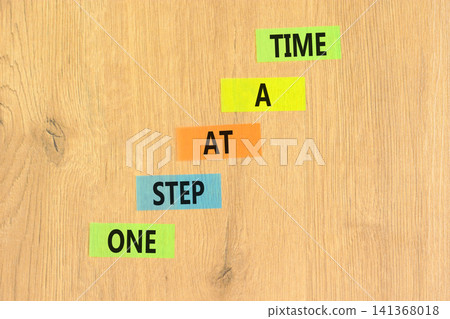One step at a time symbol. Concept words One step at a time on beautiful colored papers. Beautiful wooden background. Business and one step at a time concept. Copy space. One step at a time symbol. Concept words One step at a time on beautiful colored papers. Beautiful wooden background. Business and one step at a time concept. Copy space. 141368018