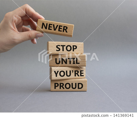 Never Stop symbol. Wooden blocks with words Never Stop Until You are Proud. Businessman hand. Beautiful grey background. Business and Never Stop concept. Copy space Never Stop symbol. Wooden blocks with words Never Stop Until You are Proud. Businessman hand. Beautiful grey background. Business and Never Stop concept. Copy space 141369141