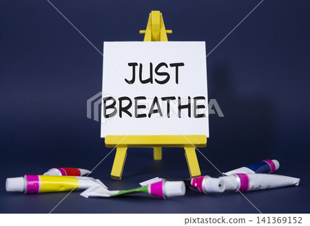 Just Breathe symbol. Wooden blocks with words Just Breathe. Beautiful deep blue background with paints and easel. Business and Just Breathe concept. Copy space. Just Breathe symbol. Wooden blocks with words Just Breathe. Beautiful deep blue background with paints and easel. Business and Just Breathe concept. Copy space. 141369152