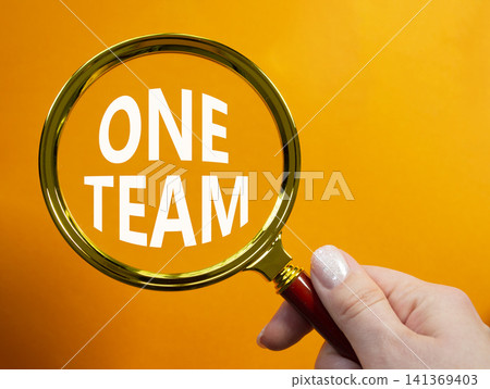 One Team symbol. Magnifying Glass with words One Team. Businessman hand. Beautiful orange background. Business and One Team concept. Copy space. One Team symbol. Magnifying Glass with words One Team. Businessman hand. Beautiful orange background. Business and One Team concept. Copy space. 141369403