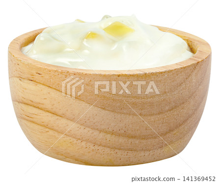 Creamy white yogurt with yellow fruit chunks served in a small round wooden bowl isolated. Healthy dairy product, breakfast snack, or cooking ingredient concept. 141369452