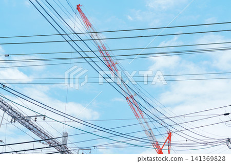 A crane stands against a blue sky with a complex network of intersecting power lines. A crane stands against a blue sky with a complex network of intersecting power lines. 141369828