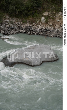 Natural river scene: large gray boulder partially submerged in rushing turquoise-white water, nature concept. Natural river scene: large gray boulder partially submerged in rushing turquoise-white water, nature concept. 141369998