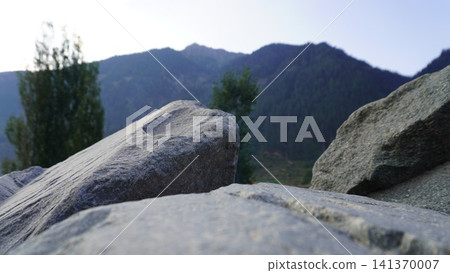 Close-up of large gray granite boulders in the foreground with forested mountains behind, scale concept. Close-up of large gray granite boulders in the foreground with forested mountains behind, scale concept. 141370007