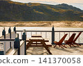 terrace of a house by the water on a sunny autumn day in Teriberka, sandy beach, mountain view, tables and chairs on the terrace, deck chairs, Murmansk region, Russia, Kola 141370058