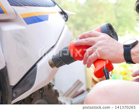 Woman using heat gun to repair plastic body of scooter. Mechanic working on vehicle maintenance. Professional equipment for auto repair and restoration. Industrial service concept. 141370265