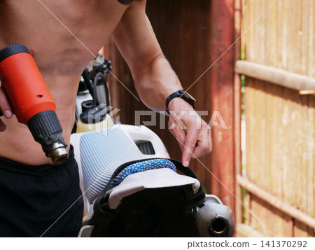 Man using heat gun to mold plastic motorcycle part. Mechanic repairing bike components with hot air tool. Industrial maintenance and custom vehicle modification process in workshop. Man using heat gun to mold plastic motorcycle part. Mechanic repairing bike components with hot air tool. Industrial maintenance and custom vehicle modification process in workshop. 141370292