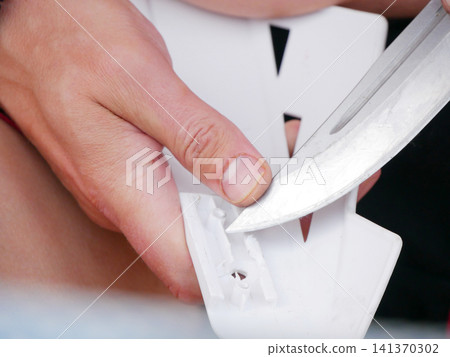 Man using sharp knife to cut white plastic part. Manual technician working with tool to trim component for repair or modification. Industrial craft and precision workshop maintenance work. Man using sharp knife to cut white plastic part. Manual technician working with tool to trim component for repair or modification. Industrial craft and precision workshop maintenance work. 141370302