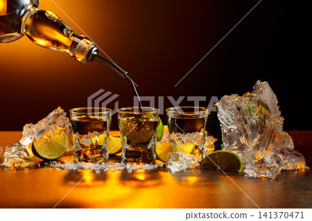 The tequila is poured from the bottle into shot glasses. The tequila is poured from the bottle into shot glasses. 141370471