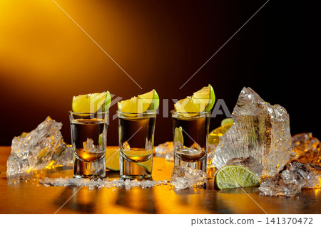 The tequila is poured from the bottle into shot glasses. 141370472