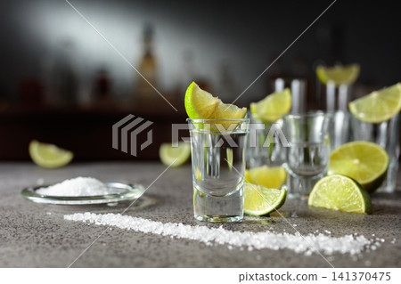 Tequila with salt and lime wedges on a gray stone table in bar. Tequila with salt and lime wedges on a gray stone table in bar. 141370475