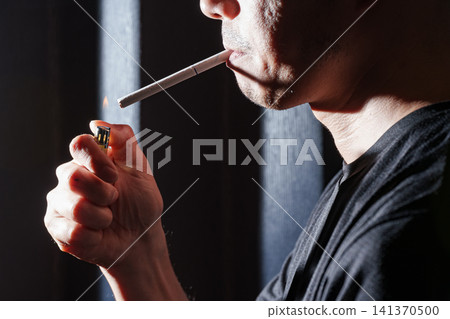 一名男子用打火機點燃嘴裡的香菸。 一名男子用打火機點燃嘴裡的香菸。 141370500