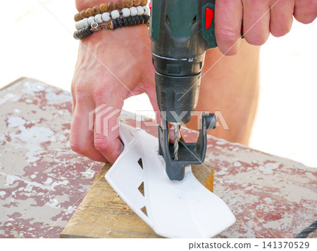 Man using electric drill to make hole in white plastic part on wooden piece. Manual worker repairing equipment. Construction, diy project and handyman home improvement concept. Man using electric drill to make hole in white plastic part on wooden piece. Manual worker repairing equipment. Construction, diy project and handyman home improvement concept. 141370529