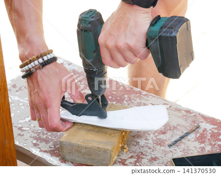 Man using electric drill to make hole in white plastic part on wooden piece. Manual worker repairing equipment. Construction, diy project and handyman home improvement concept. Man using electric drill to make hole in white plastic part on wooden piece. Manual worker repairing equipment. Construction, diy project and handyman home improvement concept. 141370530