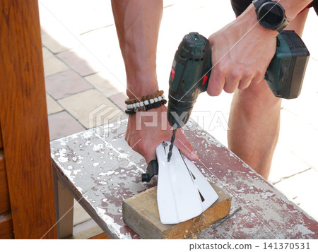 Man using electric drill to make hole in white plastic part on wooden piece. Manual worker repairing equipment. Construction, diy project and handyman home improvement concept. Man using electric drill to make hole in white plastic part on wooden piece. Manual worker repairing equipment. Construction, diy project and handyman home improvement concept. 141370531