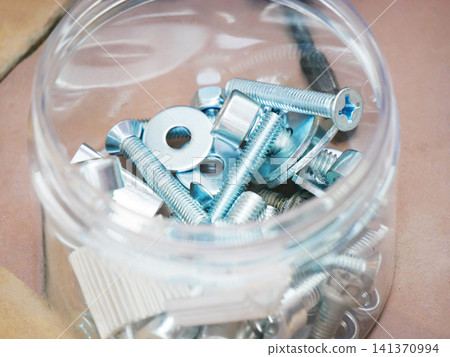Assorted metal screws, bolts, nuts and washers inside a transparent plastic container. Hardware set for repair, construction and mechanical work. Industrial components for engineering project. 141370994