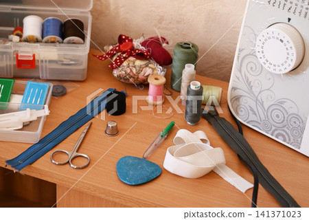 Sewing tools and materials on a desk near a sewing machine in a workspace Sewing tools and materials on a desk near a sewing machine in a workspace 141371023
