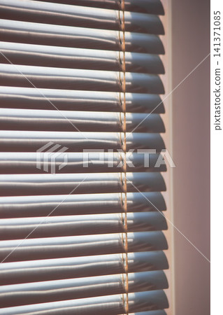 Close up of modern white window blinds filtering bright daylight Close up of modern white window blinds filtering bright daylight 141371085