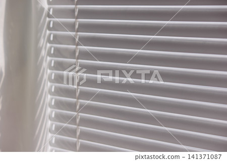 Close up of modern white window blinds filtering bright daylight Close up of modern white window blinds filtering bright daylight 141371087