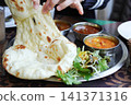 The hands of a person tearing off pieces of freshly baked naan and eating curry at an Indian restaurant. 141371316