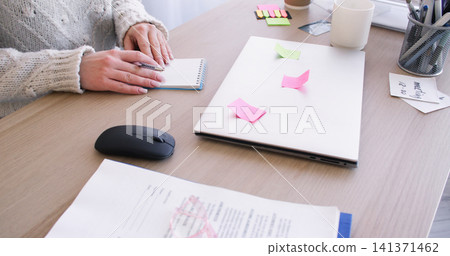 Office workflow. Freelance lifestyle. Unrecognizable female entrepreneur working at desk writing task with sticky notes on laptop indoor. Office workflow. Freelance lifestyle. Unrecognizable female entrepreneur working at desk writing task with sticky notes on laptop indoor. 141371462