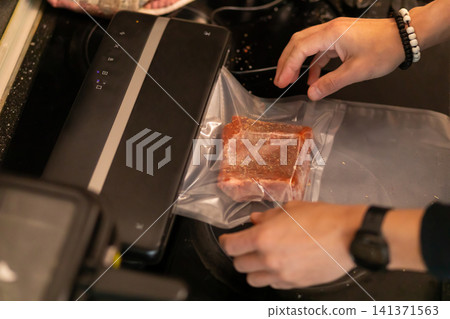 Hands Vacuum Sealing Marinated Spiced Pork Rib in Bag 141371563