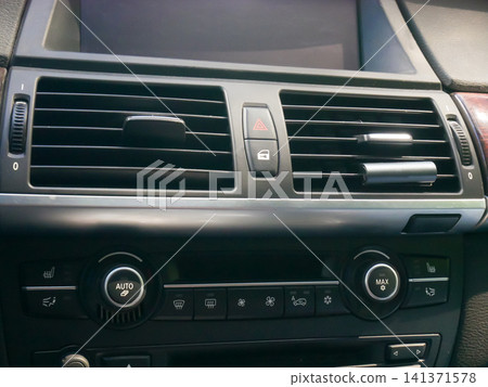 Car dashboard ventilation system with climate control panel. Interior view of automobile air conditioner vent and console buttons. Detailed view of vehicle temperature adjustment feature. Car dashboard ventilation system with climate control panel. Interior view of automobile air conditioner vent and console buttons. Detailed view of vehicle temperature adjustment feature. 141371578