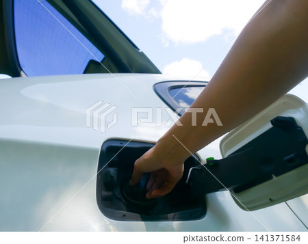 Woman opening fuel tank cap of white car to refill petrol at gas station. Transportation vehicle maintenance and driver refueling service. Daily travel routine and commute concept. Woman opening fuel tank cap of white car to refill petrol at gas station. Transportation vehicle maintenance and driver refueling service. Daily travel routine and commute concept. 141371584