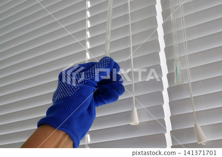 Manually adjusting white metal window blinds with cords. Controlling sunlight and providing comfort in the home. Mechanisms for opening and closing plastic horizontal shutters Manually adjusting white metal window blinds with cords. Controlling sunlight and providing comfort in the home. Mechanisms for opening and closing plastic horizontal shutters 141371701