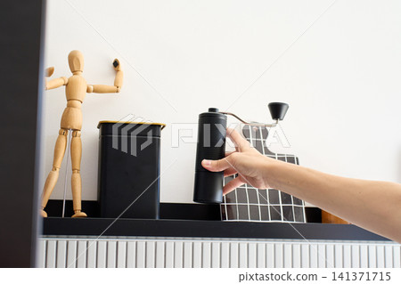 Hand takes manual coffee grinder from kitchen shelf before brewing coffee Hand takes manual coffee grinder from kitchen shelf before brewing coffee 141371715