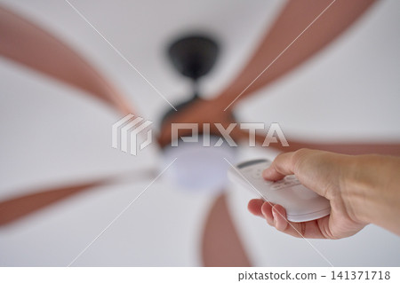 Person using remote control to operate ceiling fan mounted on white ceiling Person using remote control to operate ceiling fan mounted on white ceiling 141371718