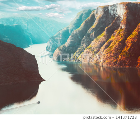 Boat sailing in a deep Norwegian fjord with steep mountain reflections. Boat sailing in a deep Norwegian fjord with steep mountain reflections. 141371728