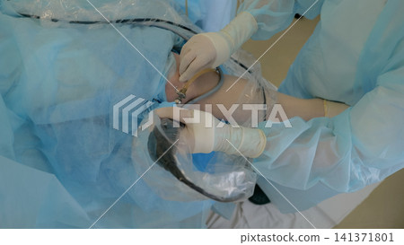 Close surgical scene with gloved medical staff treating covered patient under sterile blue drapes, focusing on hands, tubing, gauze, and protected operating room area Close surgical scene with gloved medical staff treating covered patient under sterile blue drapes, focusing on hands, tubing, gauze, and protected operating room area 141371801