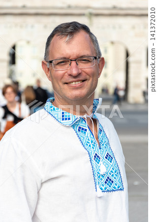 Smiling mature man wearing traditional Ukrainian embroidered vyshyvanka shirt outdoors with historic urban background for cultural, travel and lifestyle projects Smiling mature man wearing traditional Ukrainian embroidered vyshyvanka shirt outdoors with historic urban background for cultural, travel and lifestyle projects 141372010