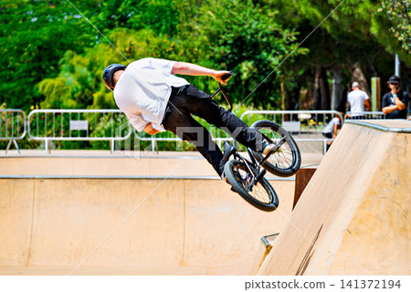 A young man practicing BMX and performing tricks at the skatepark 141372194