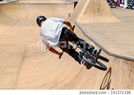 A young man practicing BMX and performing tricks at the skatepark A young man practicing BMX and performing tricks at the skatepark 141372196