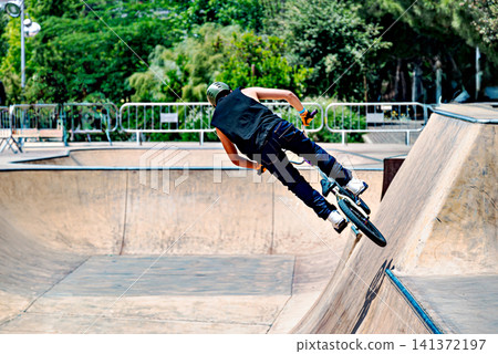 A young man practicing BMX and performing tricks at the skatepark A young man practicing BMX and performing tricks at the skatepark 141372197