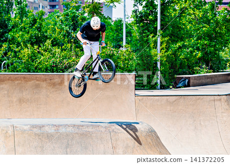 A young man practicing BMX and performing tricks at the skatepark A young man practicing BMX and performing tricks at the skatepark 141372205