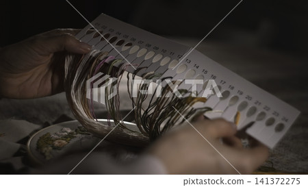 Woman Chooses Thread. Carefully Selecting Thread Shades From Numbered Color Swatches For Embroidery. Media Woman Chooses Thread. Carefully Selecting Thread Shades From Numbered Color Swatches For Embroidery. Media 141372275