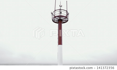 Red and white antenna mast against cloudy sky Red and white antenna mast against cloudy sky 141372356