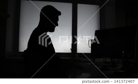 Contemplative Man By Window. Leaning Figure Of Man Lost In Thought At His Laptop Near Lit Window. Media 141372407