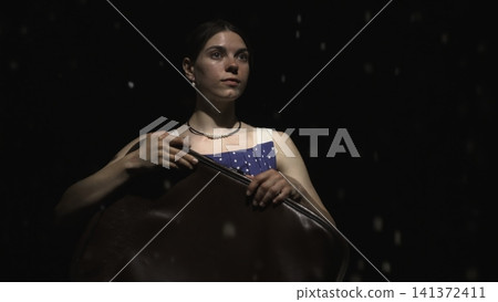 Young woman playing a string instrument on a dark stage Young woman playing a string instrument on a dark stage 141372411